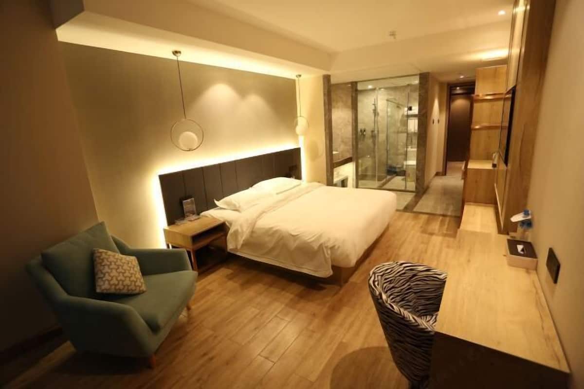 A modern hotel room with a bed, a seating area with a chair, a small table, and a shower area.