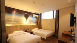 A hotel room with two beds, a wooden headboard, a nightstand, a desk, and a window with curtains. - Jin Hao Hotel (Dunhua)