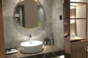 A bathroom with a round mirror, a white sink, and toiletries on the counter. - Jin Hao Hotel (Dunhua)