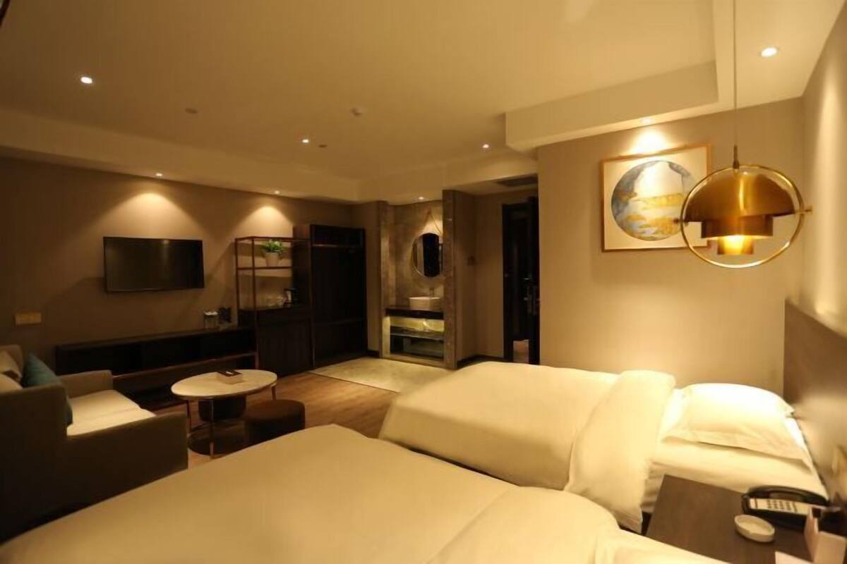 A hotel room with a bed, a sofa, a small table, a TV, and a bathroom visible through an open door.