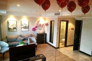 A living room with a sofa, a TV, and a plant. There are balloons hanging from the ceiling. - Jin Hao Hotel (Dunhua)