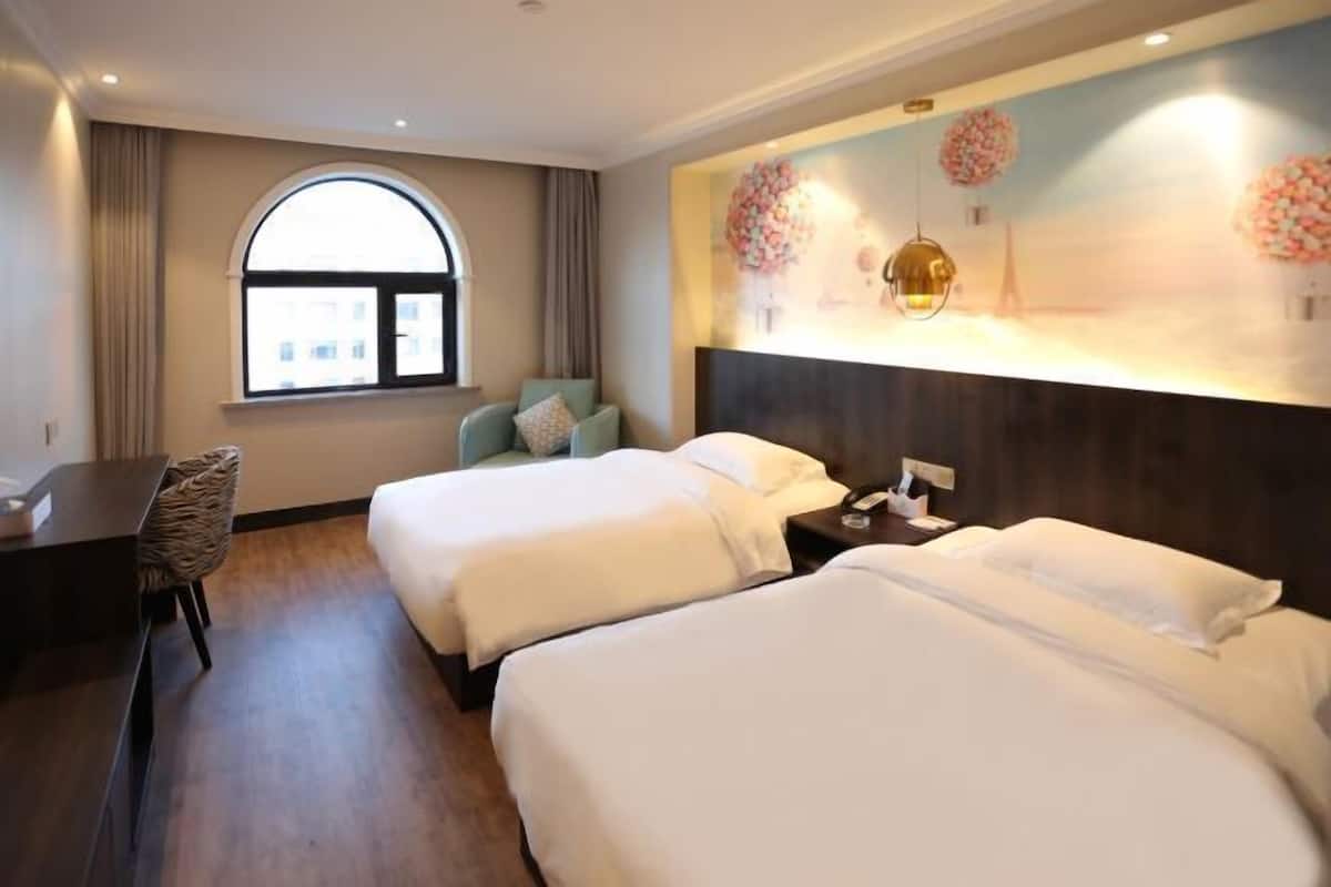 A hotel room with two beds, a desk, a chair, and a large window.