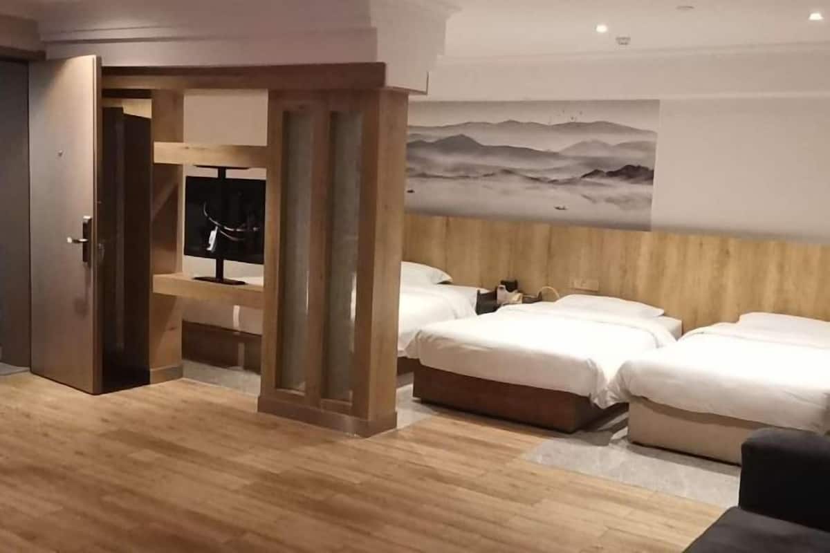 A hotel room with a wooden floor, a bed with white bedding, a wooden headboard, and a painting of mountains on the wall.