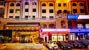A hotel with a prominent sign reading "TIN MAO HOTEL" and a lower sign for "JIN MAO HOTEL". There are multiple cars parked in front, and the building features a traditional architectural style with arched windows and a balcony on the upper floor. - Jin Hao Hotel (Dunhua)