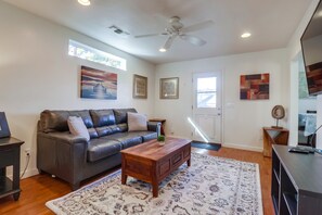 A living room with a leather sofa, wooden coffee table, patterned rug, ceiling fan, and artwork on the walls.