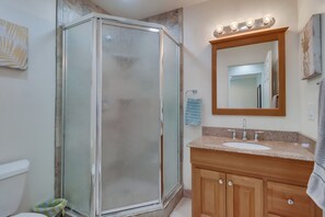 A bathroom with a glass-enclosed shower, a sink with a vanity, and a mirror with lights above it.