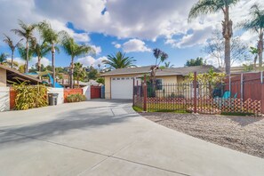 A residential area with a paved driveway leading to a garage, surrounded by palm trees and a fenced yard.