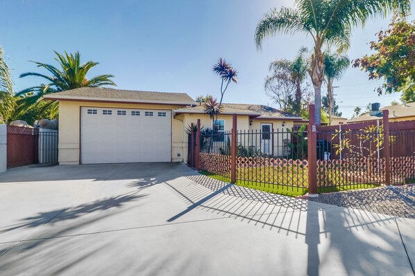 A residential property with a garage, a fenced yard, and palm trees.