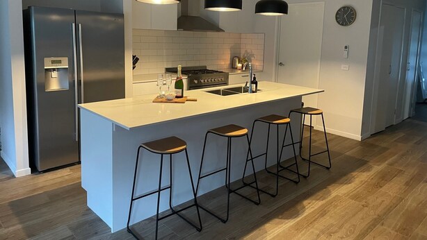 Une cuisine moderne dotée d’un îlot central, de tabourets de bar, de luminaires suspendus et d’un réfrigérateur en acier inoxydable.