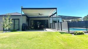 Une maison moderne dotée d’un patio couvert, d’une piscine et d’une pelouse.