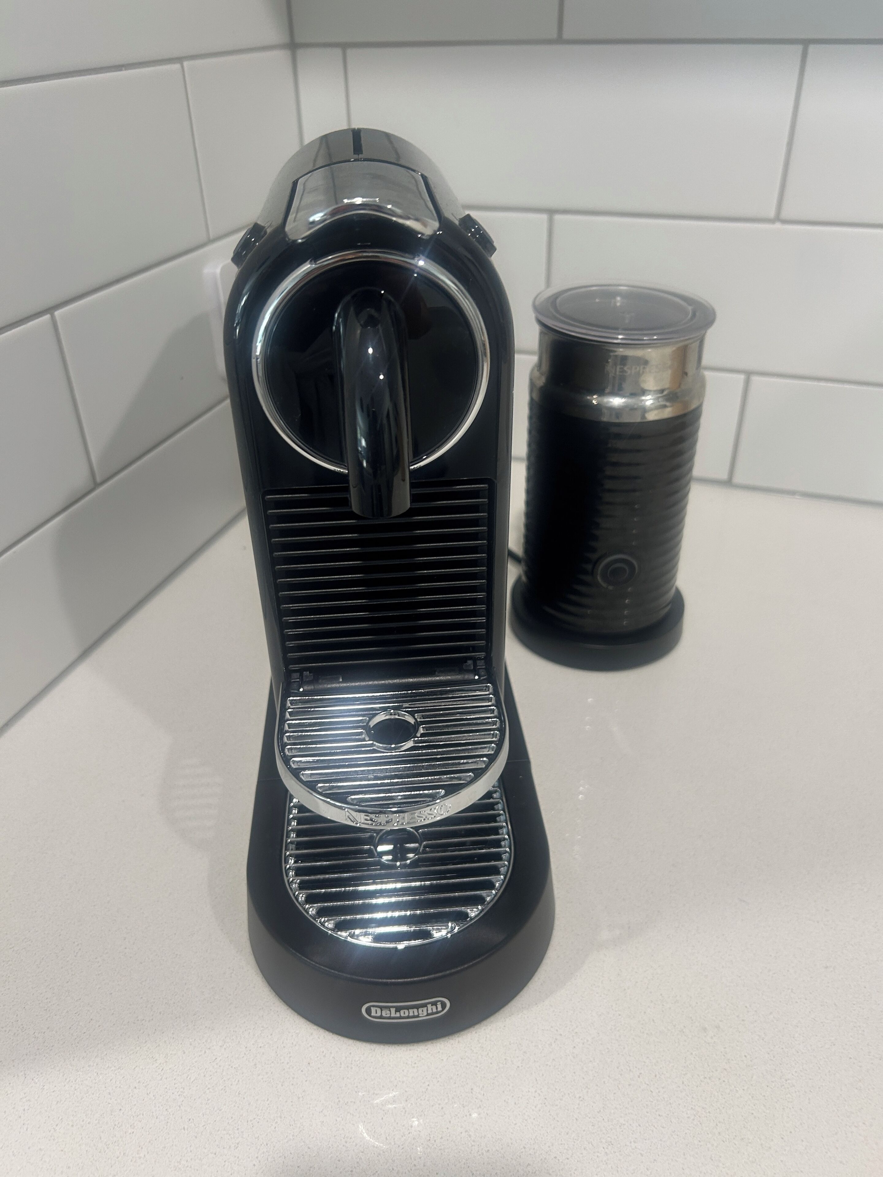 A black coffee machine with a transparent water reservoir and a black cup holder on a countertop.
