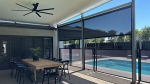 Une terrasse extérieure moderne dotée d’une piscine, d’un espace repas avec des chaises et une table, et d’un ventilateur de plafond.