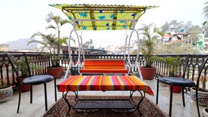 A balcony with a swing seat, potted plants, and a view of the cityscape. - The Leef Inn (Abu Road)