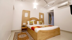 A bedroom with a wooden bed, a nightstand, a wall-mounted air conditioner, and a ceiling fan. - The Leef Inn (Abu Road)