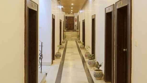 A long, narrow hallway with wooden ceiling and white walls, flanked by doors and potted plants. - The Leef Inn (Abu Road)