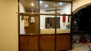 A reception area with a wooden counter, a person behind it, and potted plants. - The Leef Inn (Abu Road)