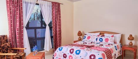 A bedroom with a large bed, a wooden chair, a small table, and a window with curtains.