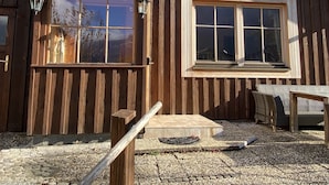 Eine rustikale Holzhütte mit einem grünen Dach, großen Fenstern und einem Eingang mit Pflastersteinen.