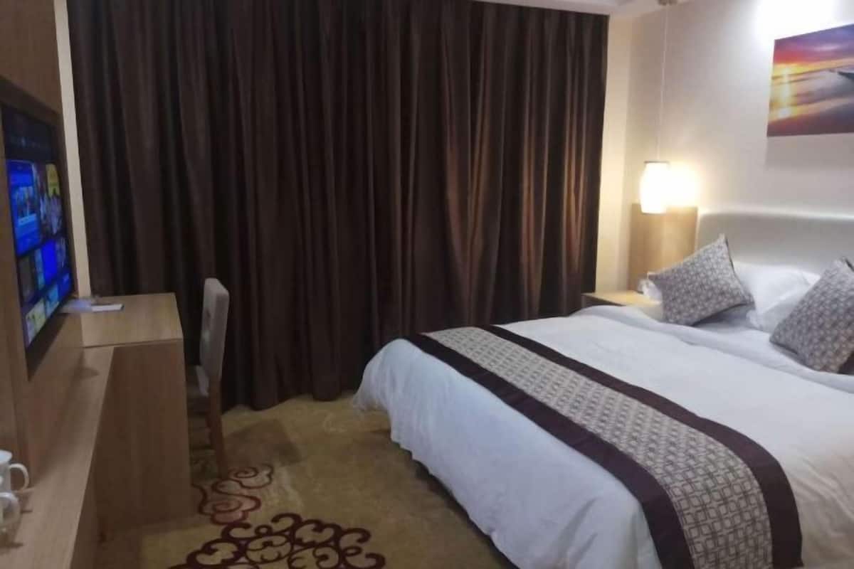 Hotellihuone, jossa on sänky, työpöytä, televisio ja verho.