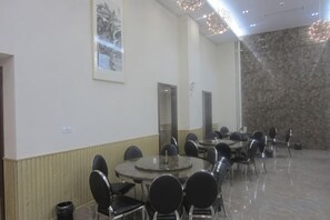 Un salón de conferencias con varias mesas y sillas, una pared de mármol y un cuadro en la pared.