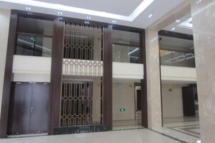 Un vestíbulo moderno con una columna central, puertas de vidrio y piso de mármol.
