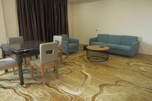 Un salon avec une table en bois foncé, deux fauteuils bleu clair, un canapé bleu et une table basse ronde dont le piétement est constitué d’une structure en fil métallique noir.