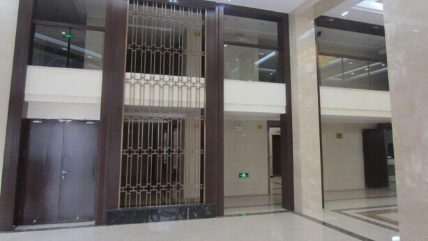 Een moderne hotel lobby met een centrale kolom, glazen deuren en een gepolijste vloer.