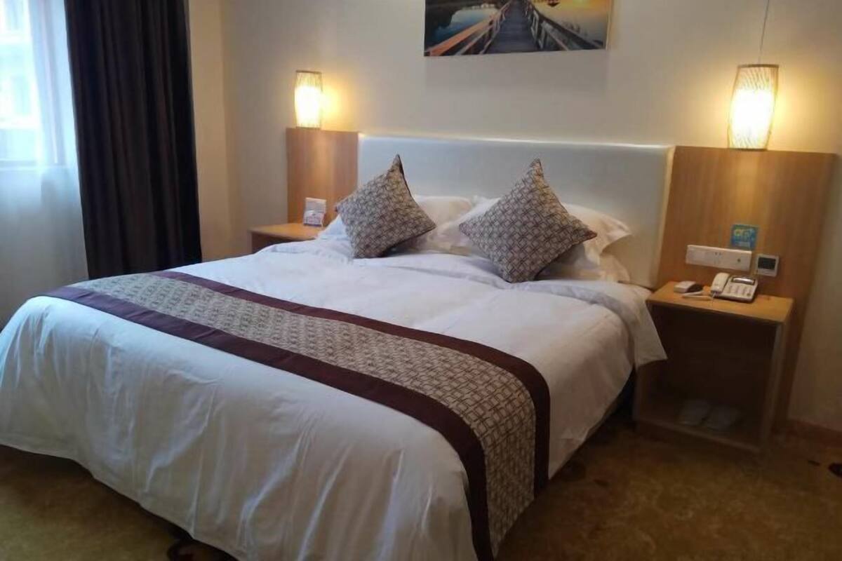 Hotellihuone, jossa on suuri sänky, kaksi yöpöytää valaisimineen ja taulu seinällä.