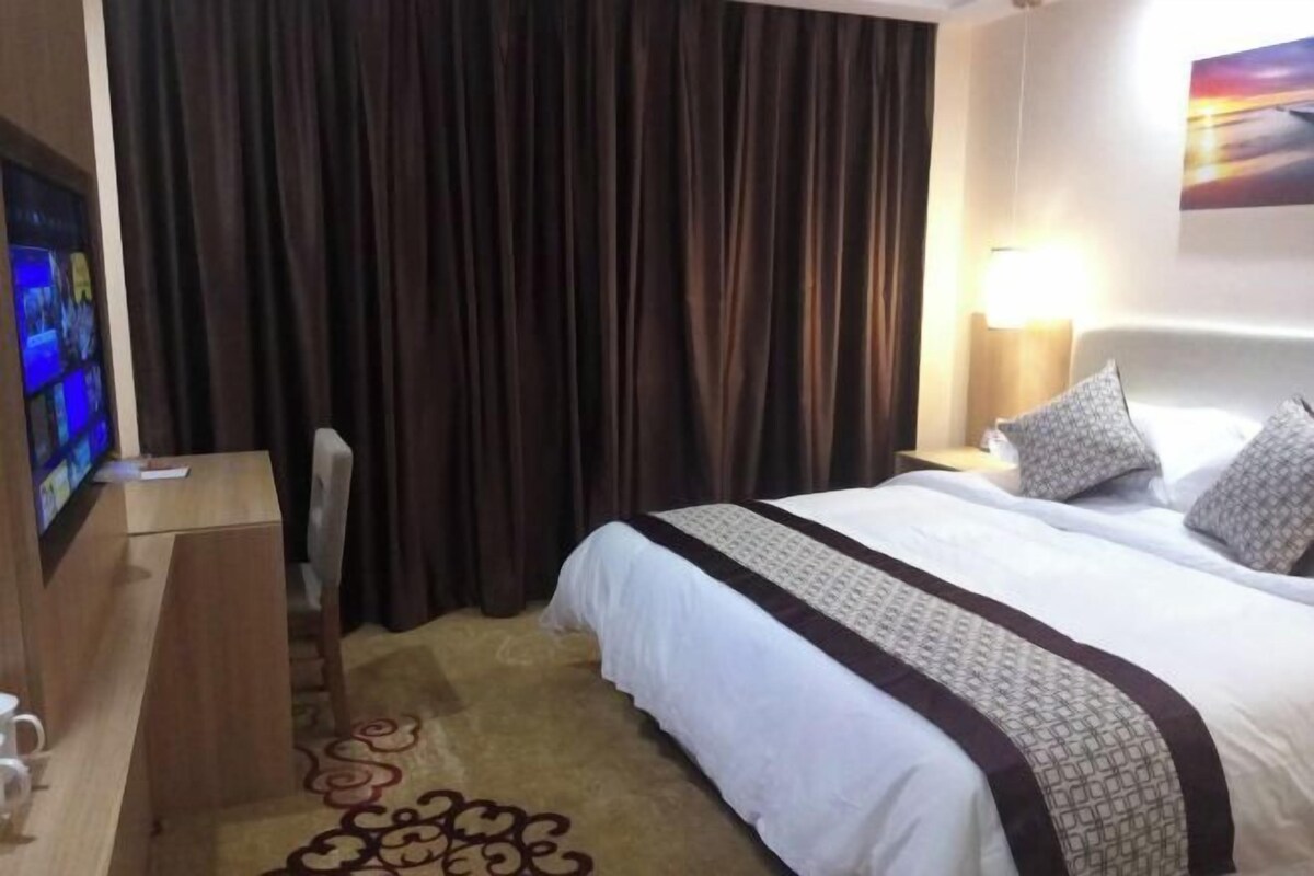Ein Hotelzimmer mit Bett, Schreibtisch, Fernseher und Vorhang.