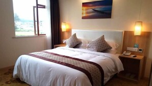 Een hotelkamer met een groot bed, twee nachtkastjes, een schilderij aan de muur en een raam met gordijnen.