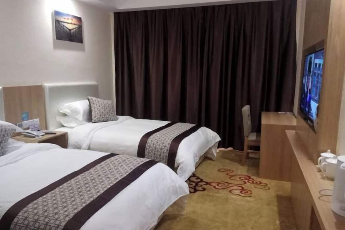 Hotellihuone, jossa on kaksi sänkyä, televisio, työpöytä ja suuri ikkuna, jossa on verhot.