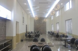 Una espaciosa sala de conferencias con múltiples mesas y sillas, techos altos con lámparas geométricas y grandes ventanales que permiten la entrada de luz natural.