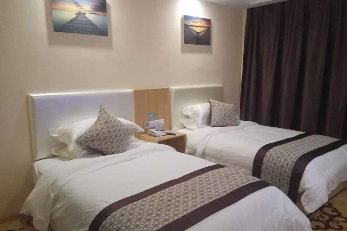 Hotellihuone, jossa on kaksi sänkyä. Jokaisessa sängyssä on pääty, yöpöytä ja seinään kiinnitetty valaisin.