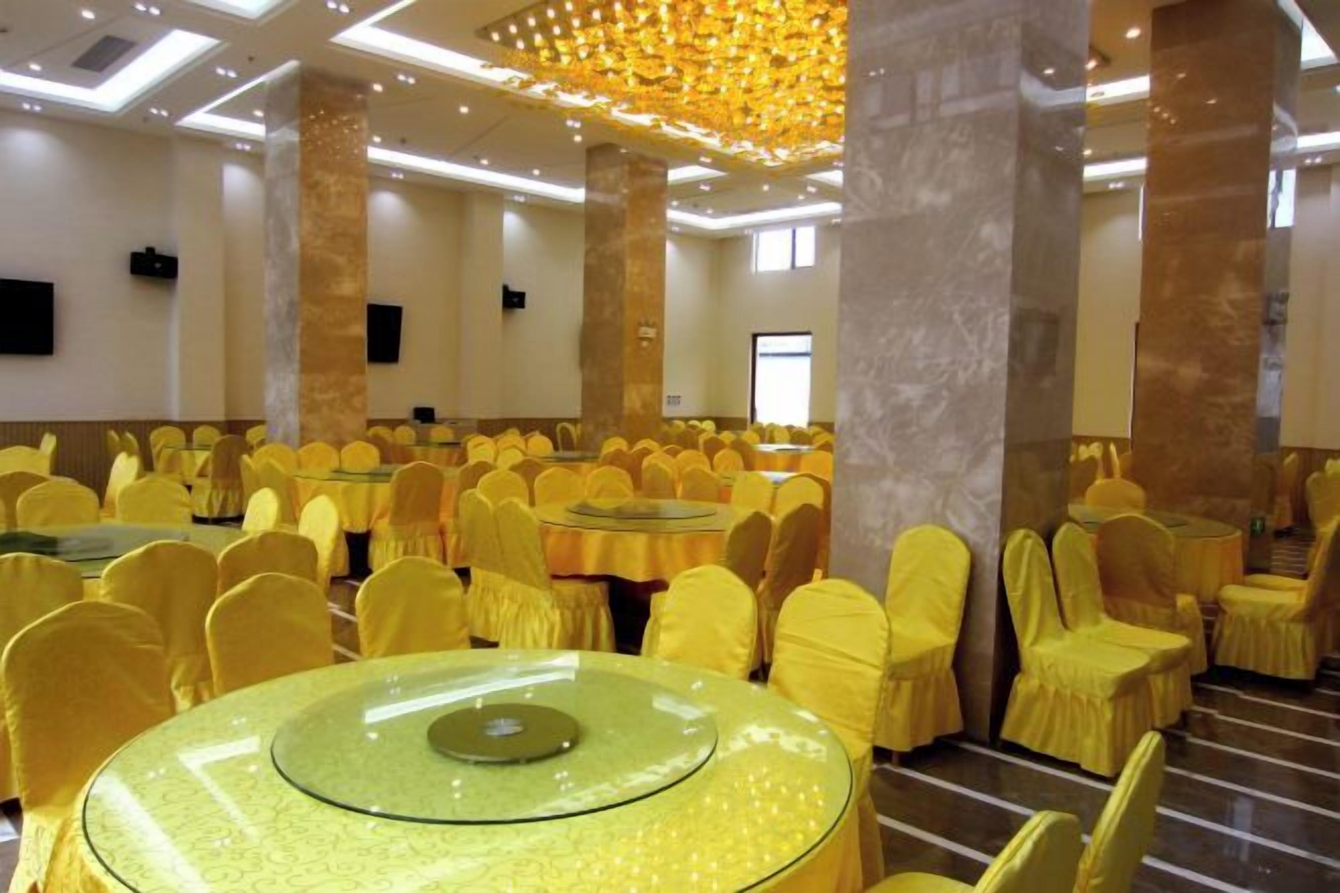 A banquet hall with round tables and chairs, high ceilings, and a modern chandelier.