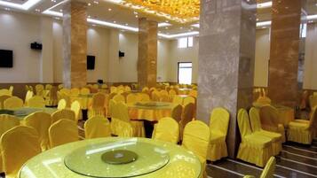 A banquet hall with round tables and chairs, high ceilings, and a modern chandelier.
