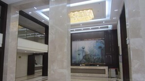Een moderne lobby met een hoge plafond, een kroonluchter, een receptiebalie en een groot kunstwerk aan de muur.