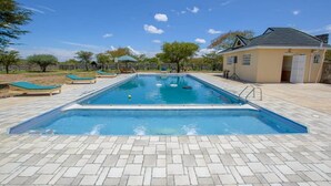A rectangular swimming pool with a tiled deck, surrounded by lounge chairs and a small building with a sloped roof. - Lomanira Splendour (Mogotio)