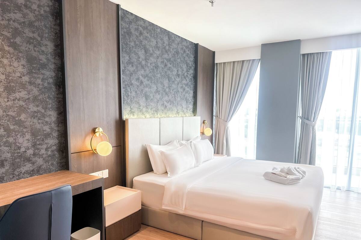 A modern hotel room with a large bed, a desk, and a nightstand.