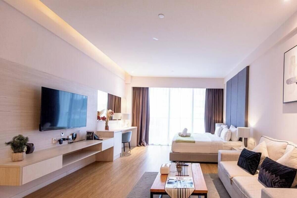 A modern hotel room with a flat-screen TV, a sofa, a coffee table, and a desk with a chair.