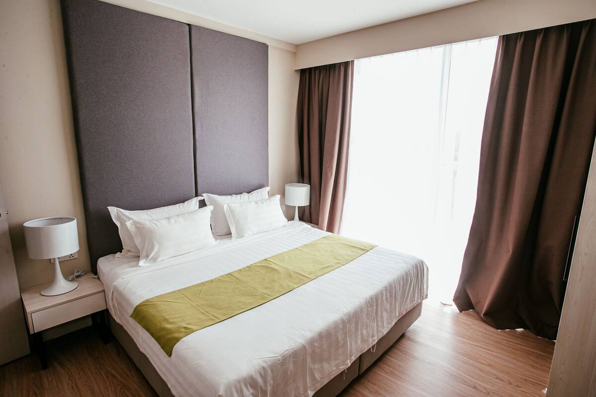A hotel room with a large bed, two bedside tables, a night lamp, and a window with curtains.