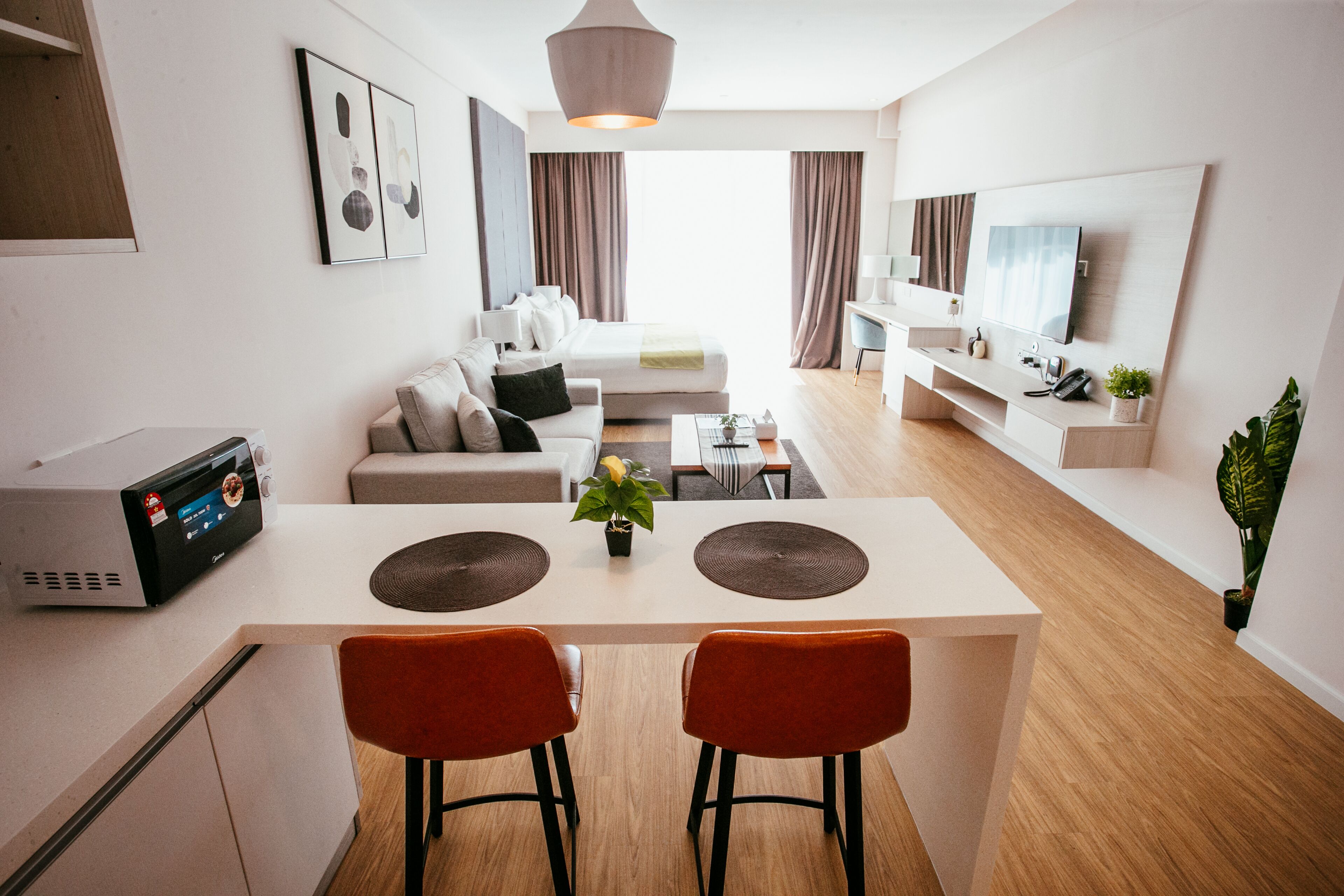 A modern hotel room with a dining area, a sofa, a TV, and a plant.