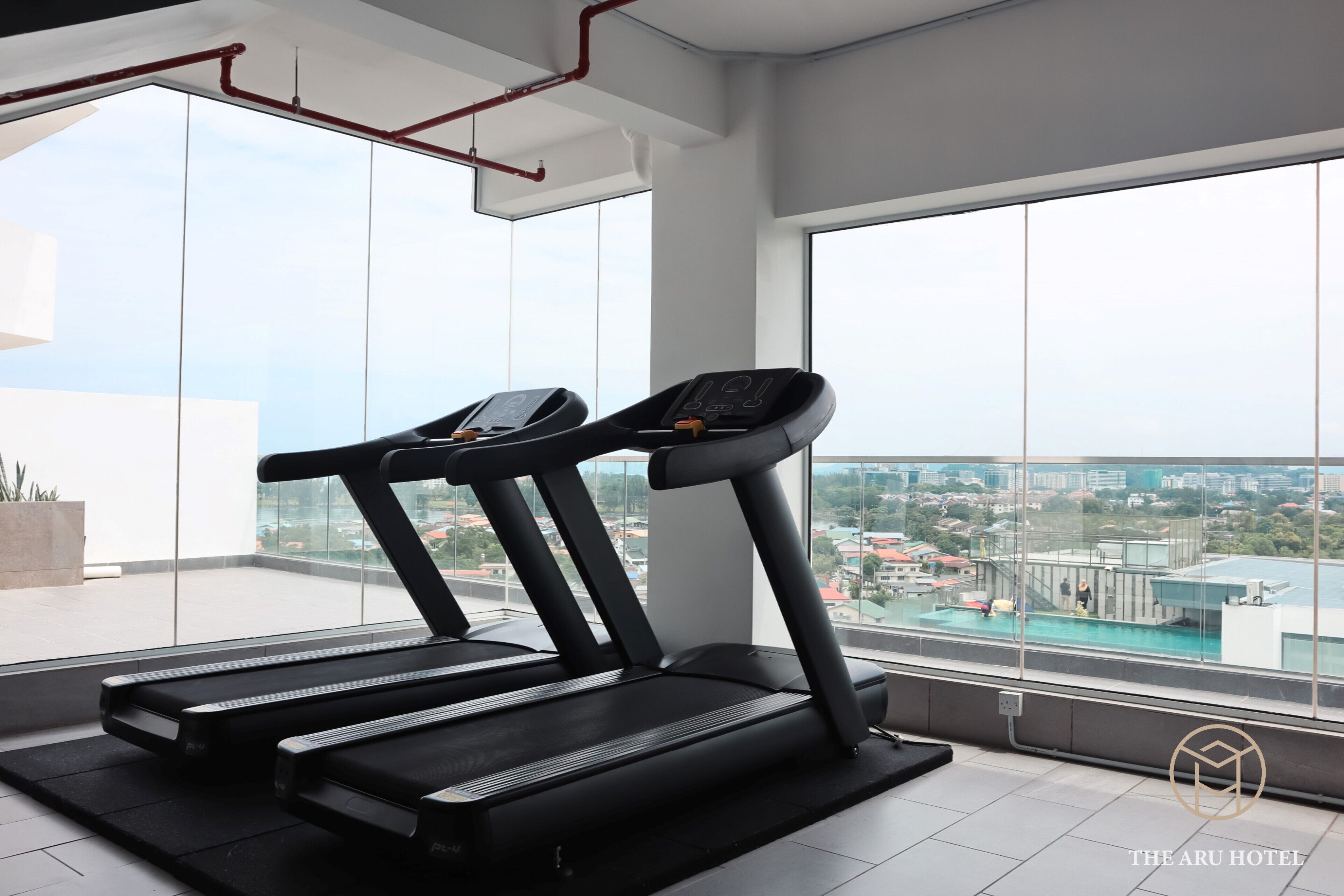 Un gimnasio con cintas de correr y un amplio ventanal con vistas a un paisaje urbano.
