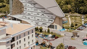 A modern building with a unique curved roof and a parking lot in front. - The Aru Hotel, Aru Suites by Ayuhouz (Kota Kinabalu)