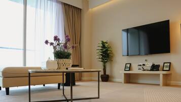 A modern living room with a sofa, a coffee table, a TV mounted on the wall, a potted plant, and a floor lamp.