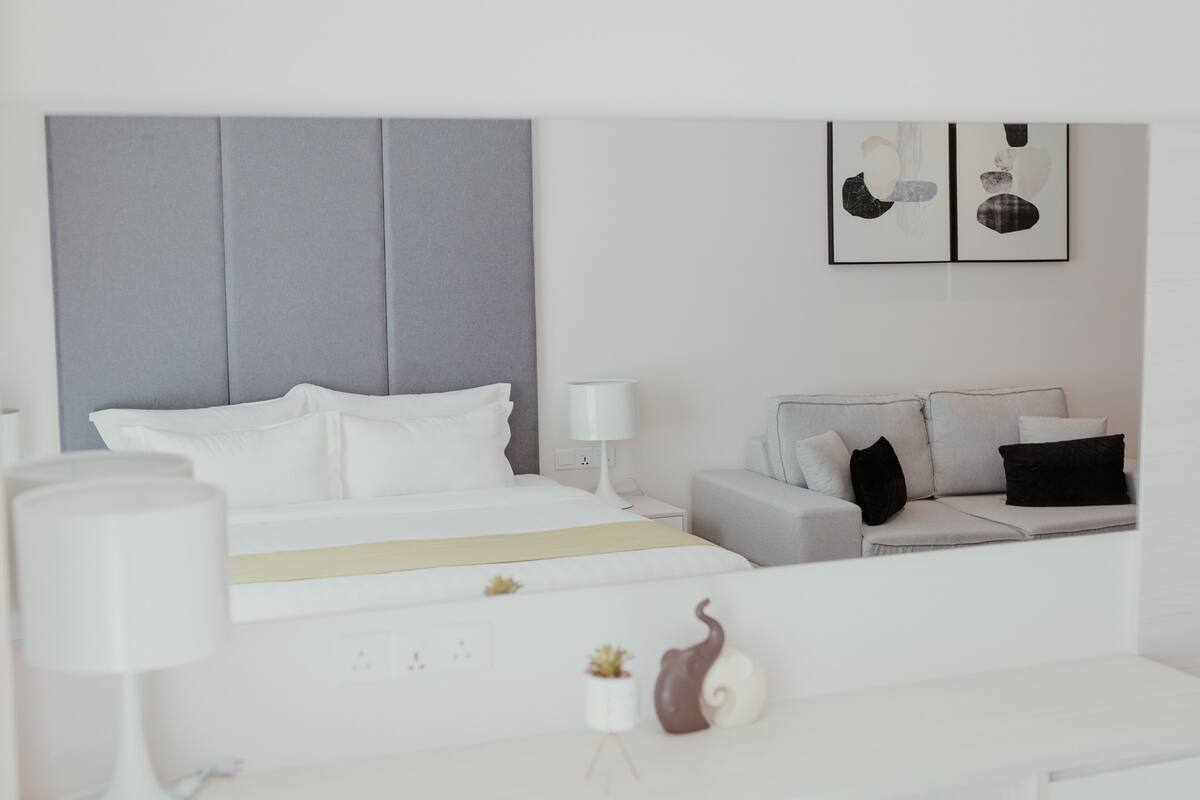 A modern hotel room with a large bed, a sofa, a bedside table with a lamp, and a small plant.
