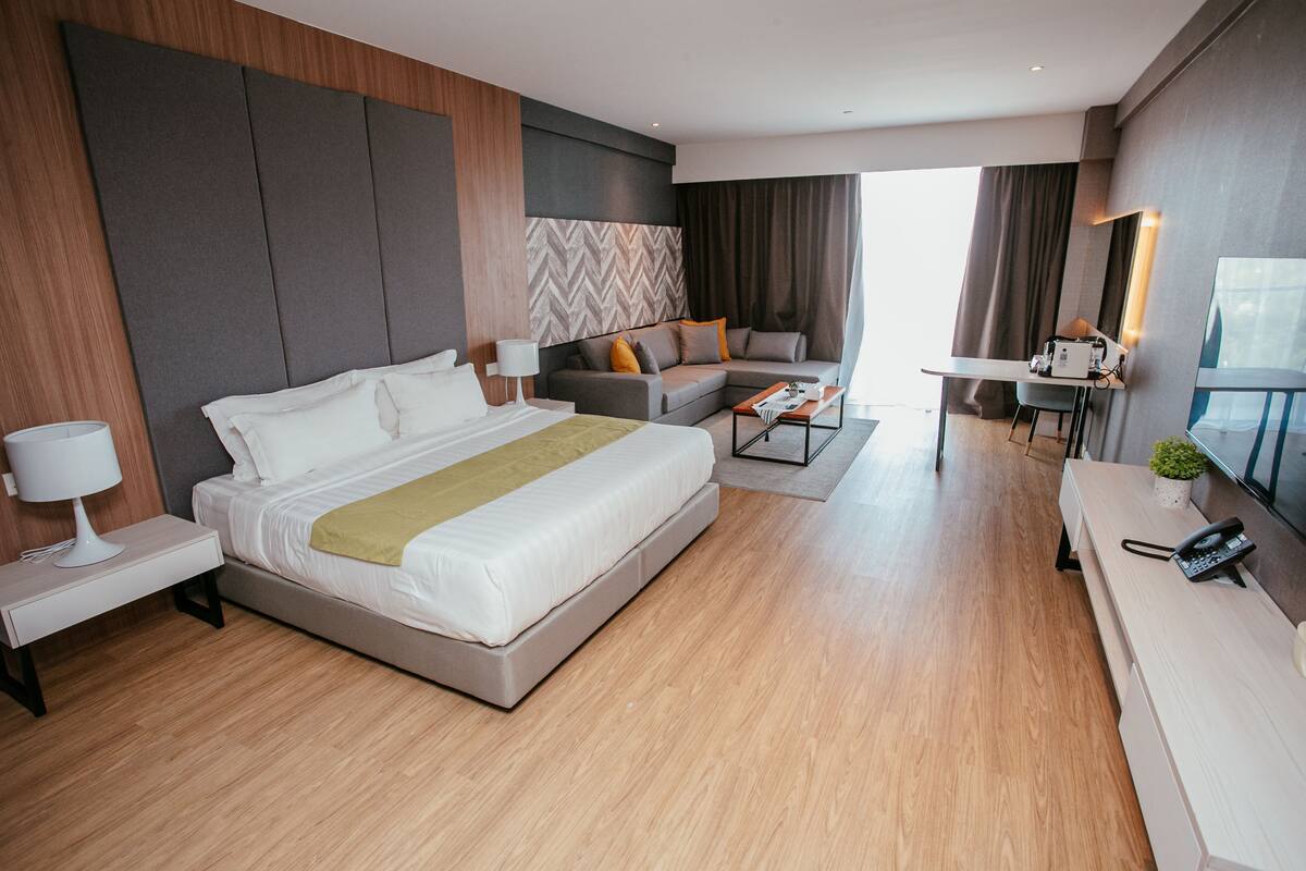 A modern hotel room with a large bed, a sofa, a desk, and a small table.