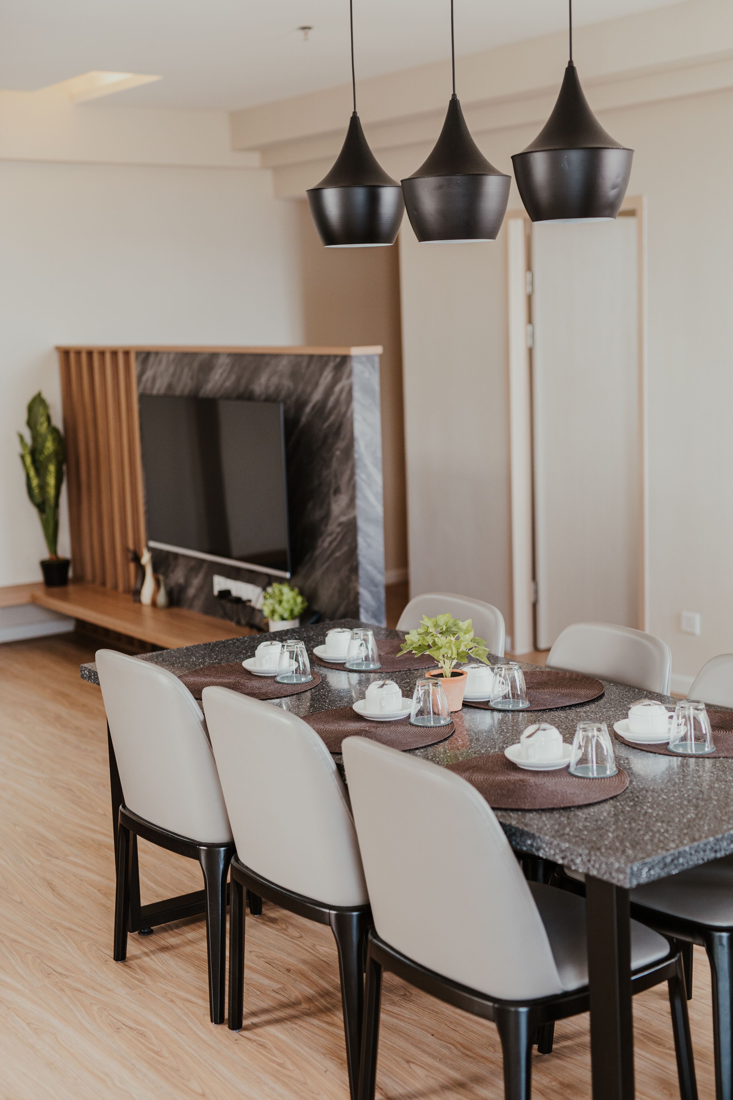 Un comedor moderno con una mesa de mármol, sillas negras y un televisor al fondo.