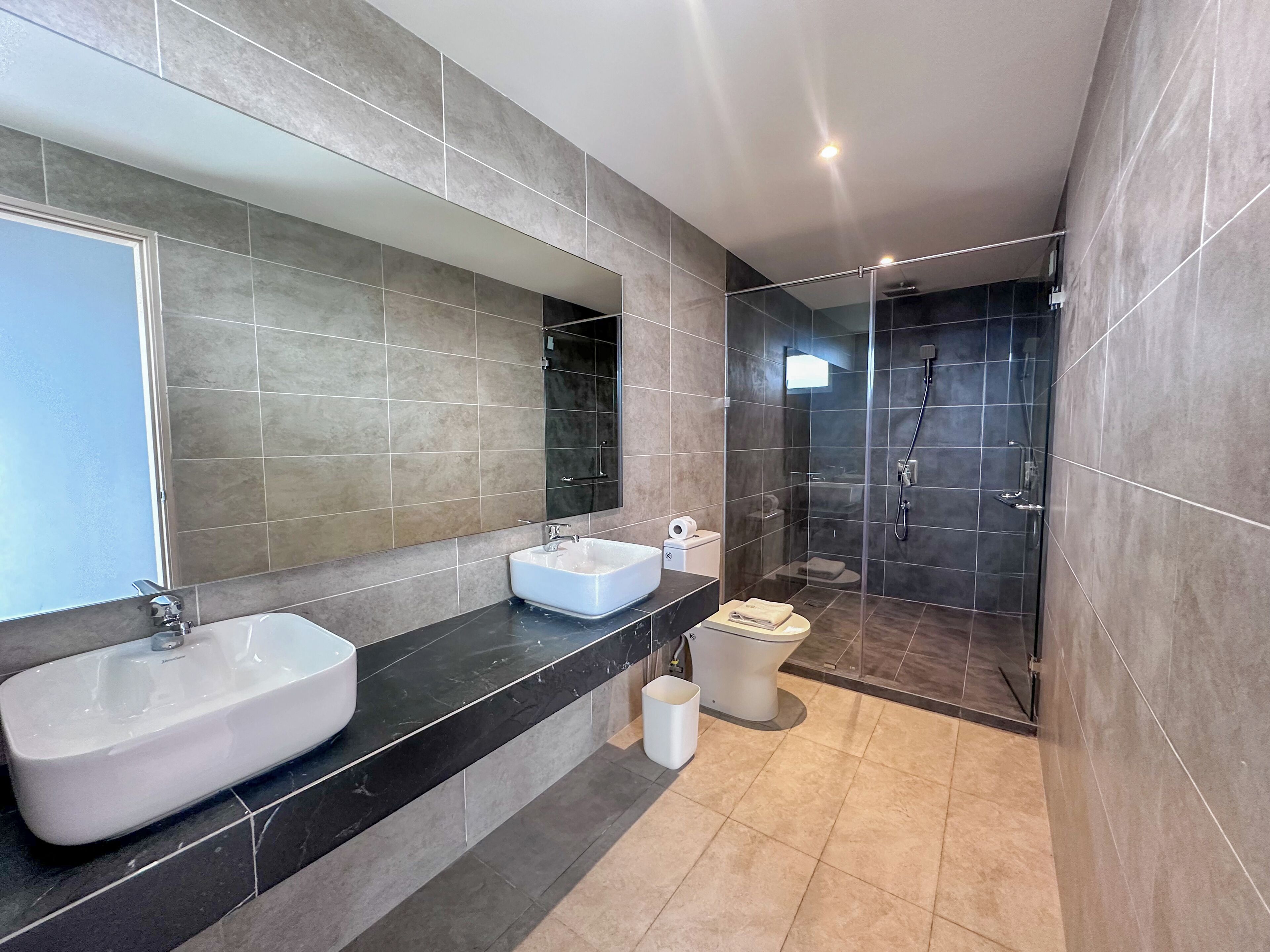 A modern bathroom with a large mirror, two sinks, a shower, and a toilet.