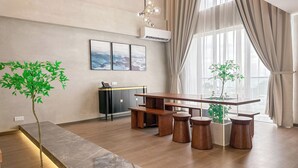 A modern living room with a long wooden table, a black and gold cabinet, and a large window with sheer curtains. - The Aru Hotel, Aru Suites by Ayuhouz (Kota Kinabalu)