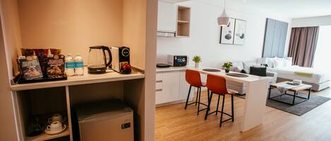 Una habitación de hotel moderna con kitchenette, un comedor con dos sillas rojas, un refrigerador pequeño y una cafetera.